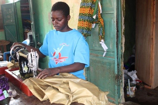 A person in a blue Foundation shirt guides fabric through a sewing machine.