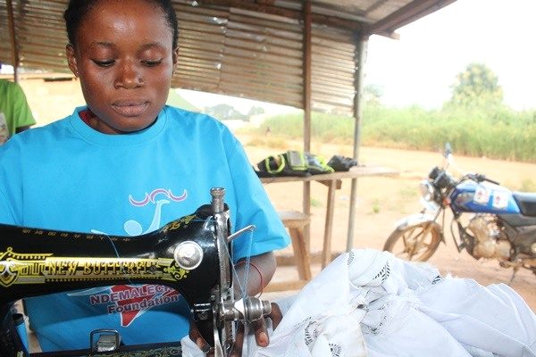 A person in a blue Foundation shirt works at a sewing machine with white fabric.