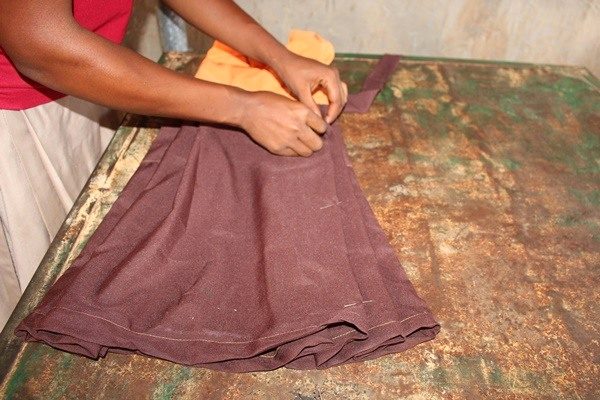Hands arrange brown fabric on a workshop table.